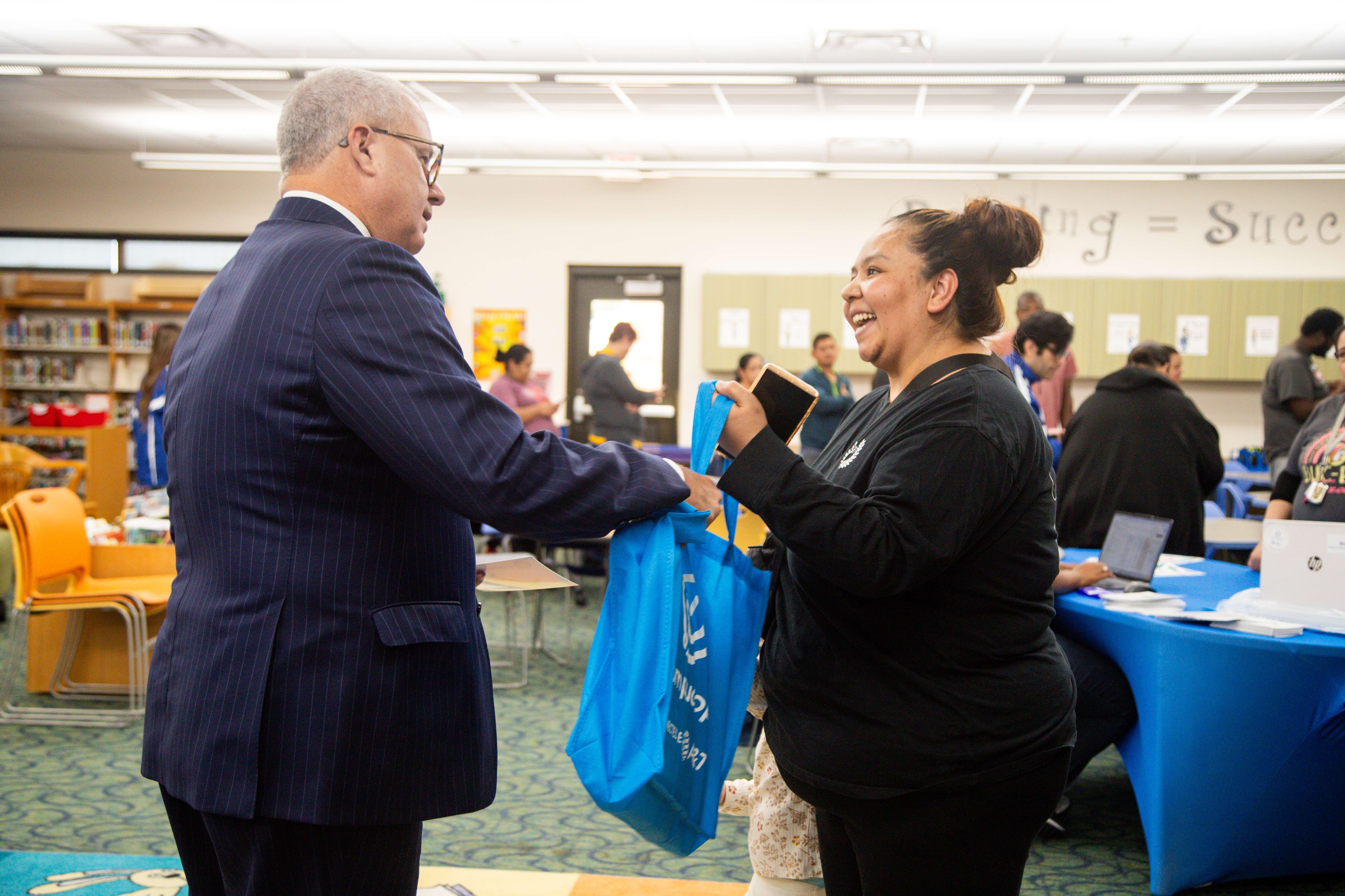 a man hands a donated laptop in a bag to a parent