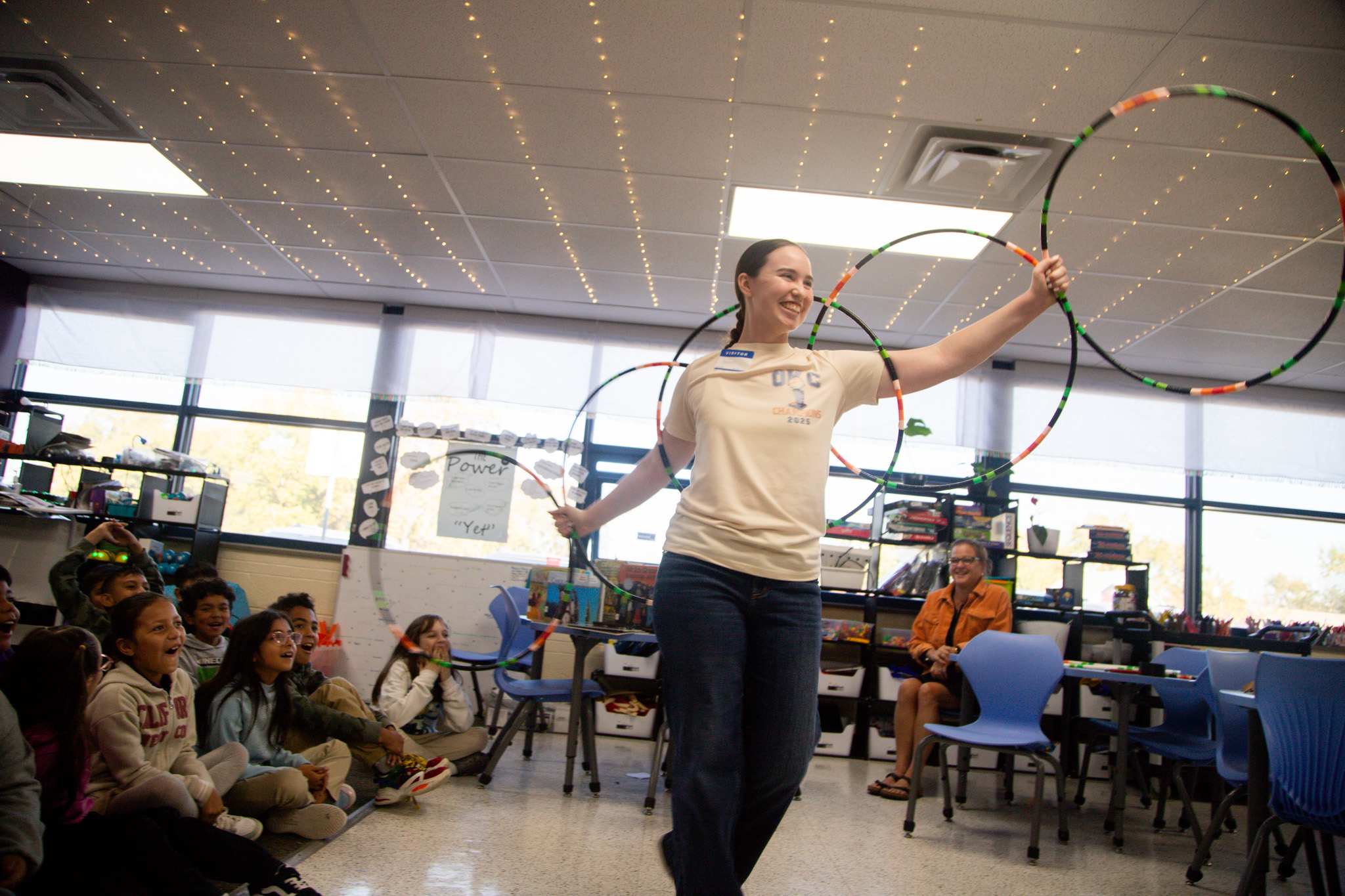 a high school student demonstrates hoop dancing for elementary students